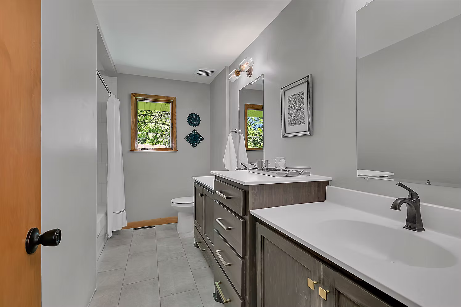 Double vanity bathroom with gray cabinets, dual mirrors, and tile floor