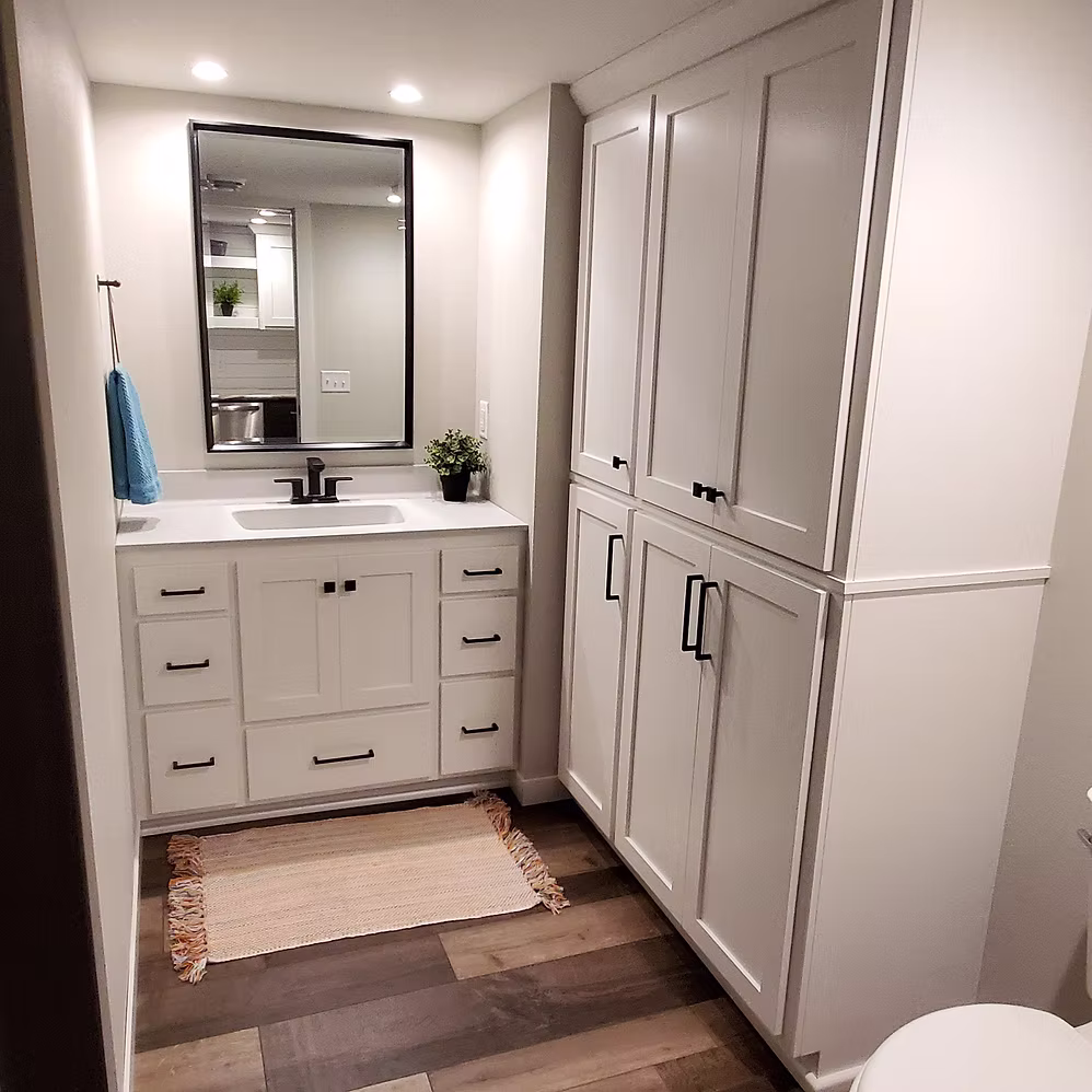 White bathroom with gray shaker vanity, linen tower, and wood-look tile floor