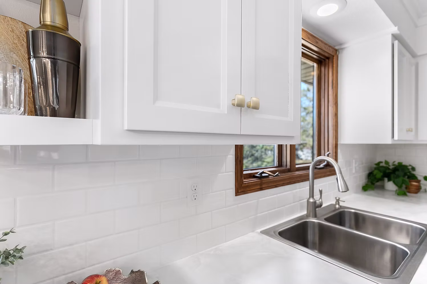 White kitchen sink with marble backsplash, wood window trim, and gold faucet