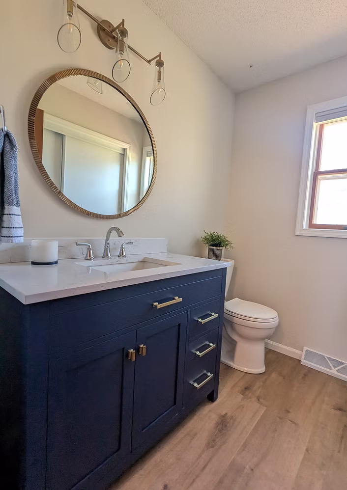 Navy blue vanity bathroom with round mirror and wood-look floor