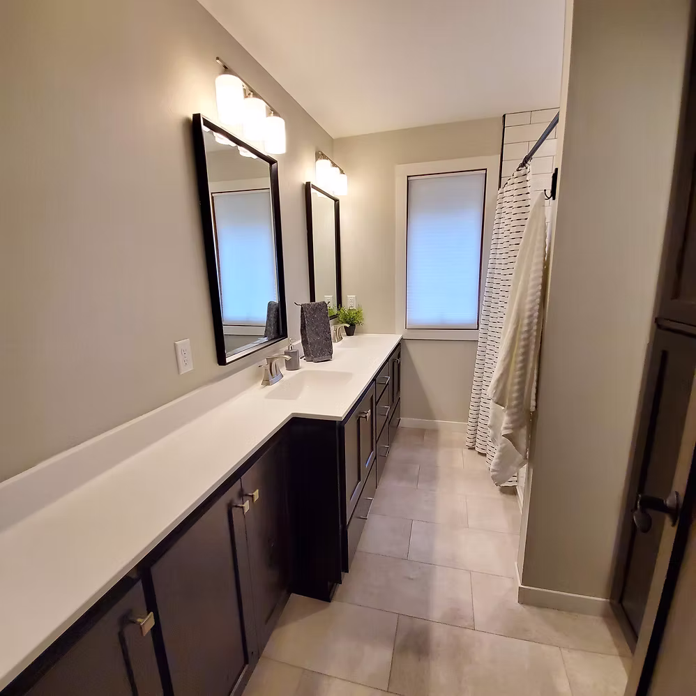 Long bathroom with dark double vanity and dual mirrors